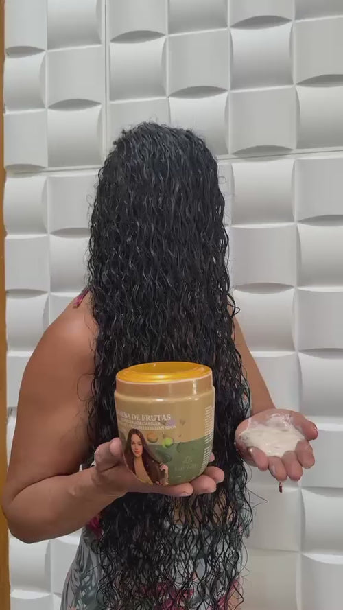 Bomba de Frutas, repolarizador capilar Eco Zelba, en la mano junto a cabello largo y rizado